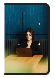 Photo of woman looking down working on a laptop in front of a blue background framed by a Ledger signer device