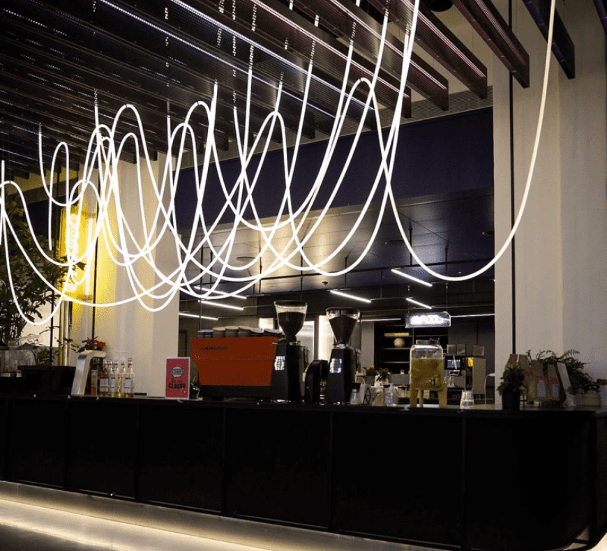 A modern coffee bar with hanging illuminated light fixtures and coffee machines on the counter