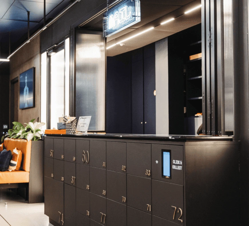 A mailroom desk with numbered lockers in front, a sign saying mail above, and an orange sofa in the distance