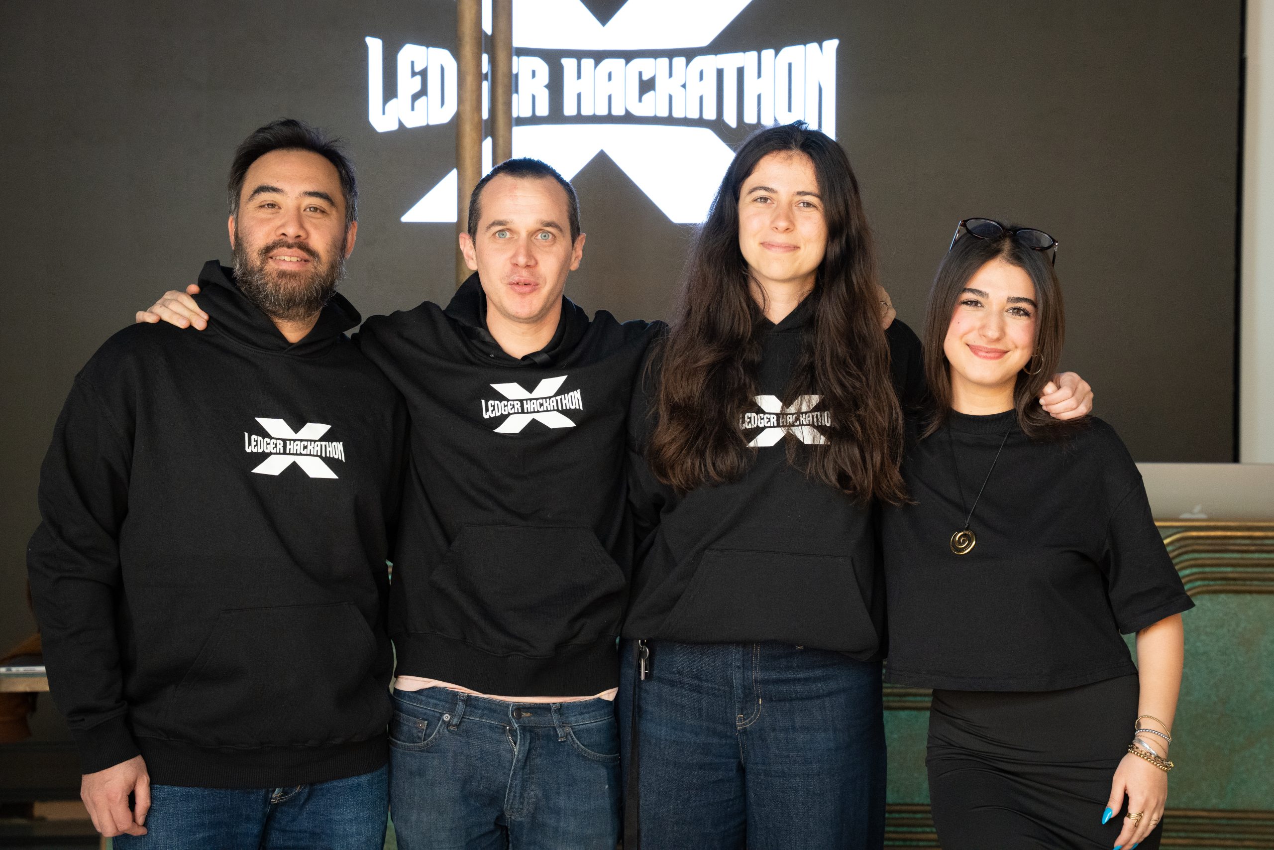 _A746020 (1) Four people in front of the ledger learning hackathon sign smiling